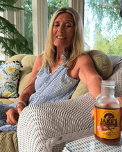 Load image into Gallery viewer, Woman enjoying Jake's StrongGinger organic pomegranate ginger drink, relaxing in a cozy setting.