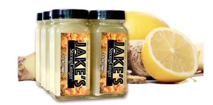 A 6 pack of Jake's StrongGinger organic ginger juice next to some ginger and lemons to depict its freshness