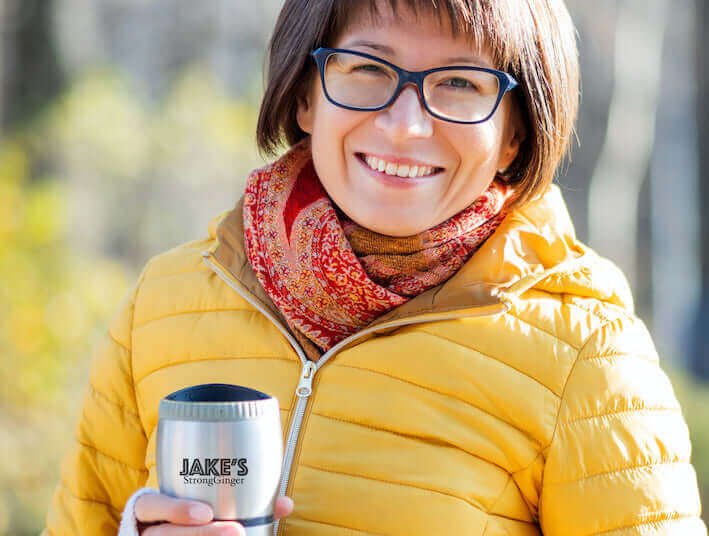 Jake's StrongGinger organic ginger juice being enjoyed in a thermal mug by a woman in a yellow puff coat.