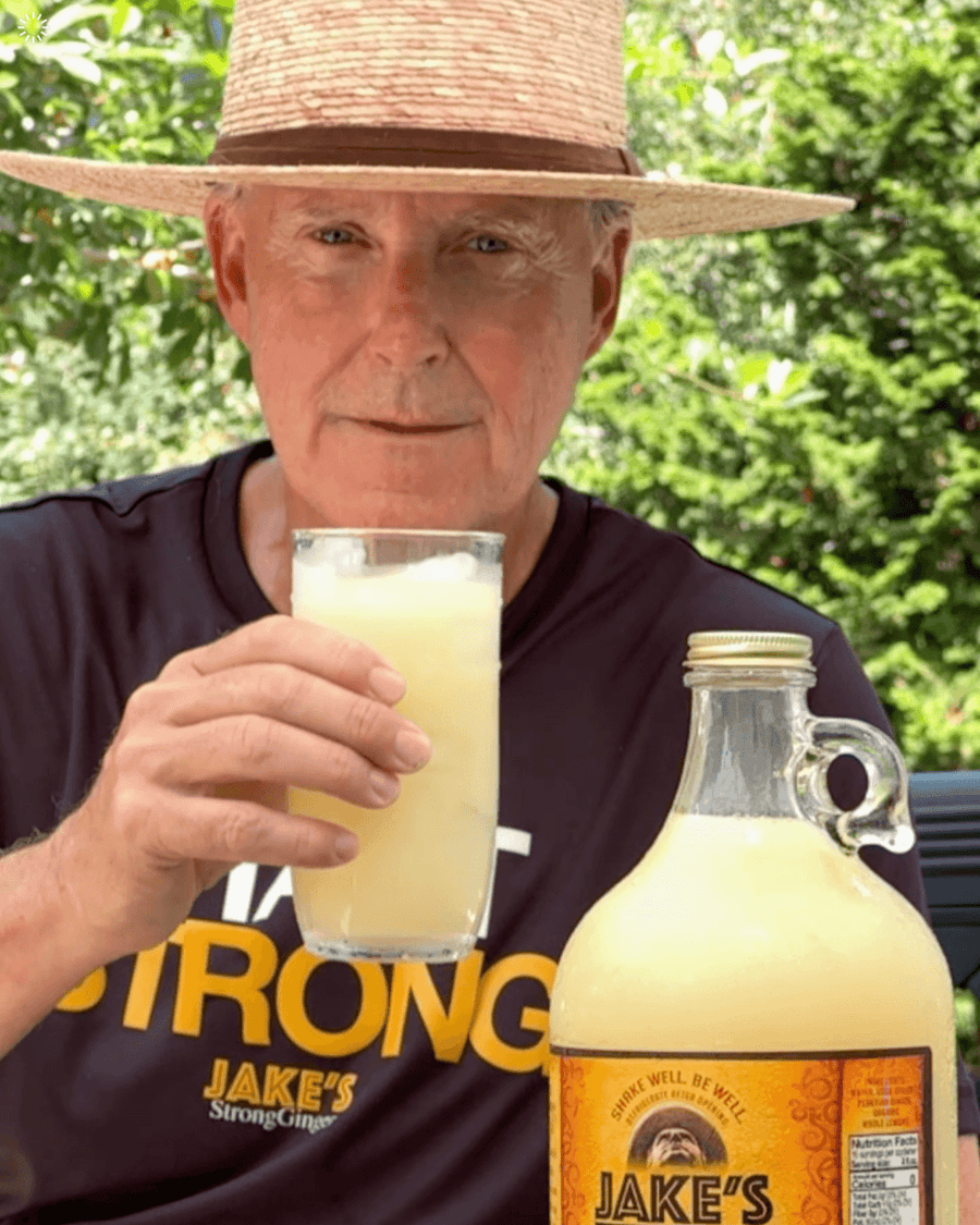 A picture of Jake in his black shirt and straw hat drinking a glass of Jake's StrongGinger organic ginger juice